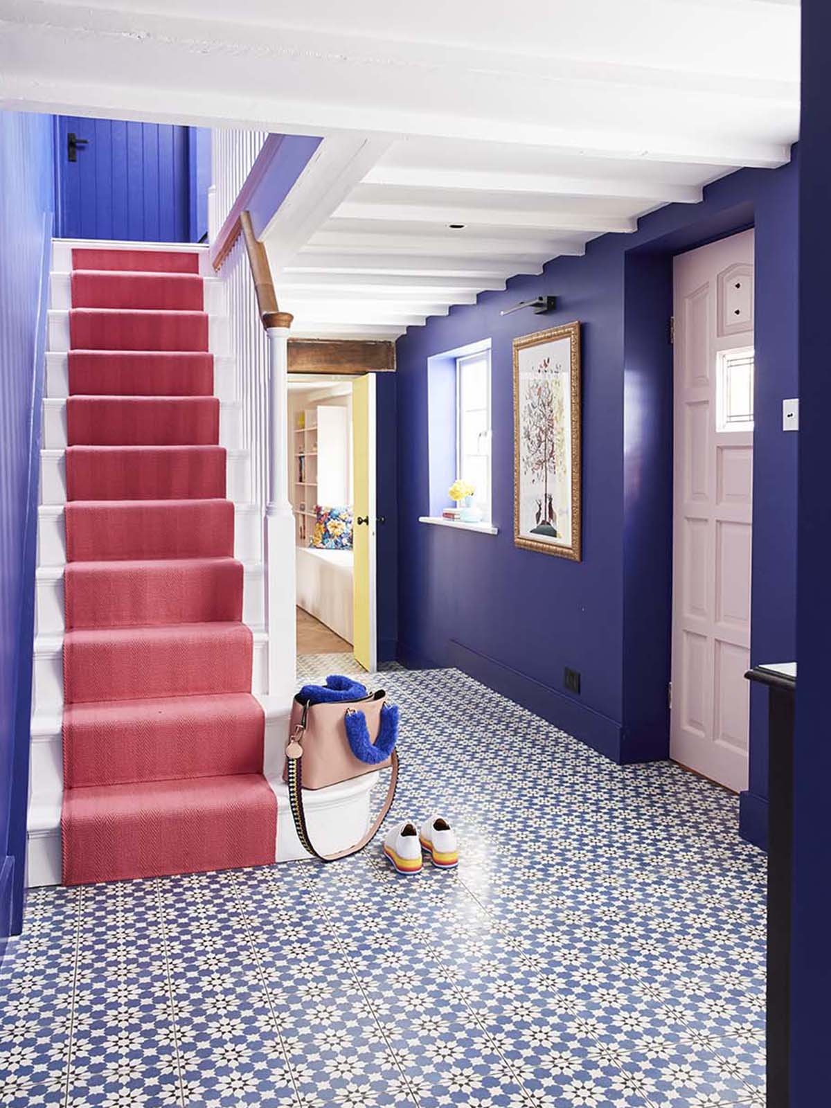 At home with interior designer Sophie Robinson. Her bright and cheery hallway has dramatic bluewalls painted in Lapis by Zoffany, blue patterned tiles by Claybrook and a bright Rose stair runner by Roger Oates