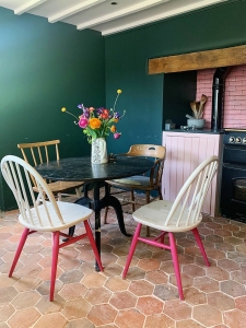 country kitchen in dark green with mid century modern ercol chairs and pink kitchen tiles. Reclaimed hexagon terracotta floor tiles complete the modern country look