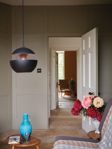 Contemporary lighting and accessories sit happily with the classic panelled wall is painted in Broccoli Brown, one of the new Farrow & Ball and Natural History Museum new colours. Sophie Robinson looks at the new paint collection here. #farrowandball #panelledwall #livingroom #sophierobinson