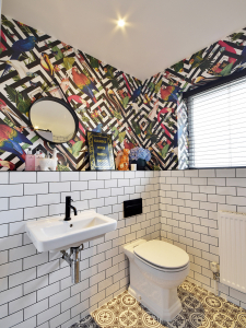 A striking bathroom featuring a geometric bird print wallpaper and white metro tile with black grout was created by interior designer Sophie Robinson for DIYSOS. #diysos #thebigbuild #sophierobinson