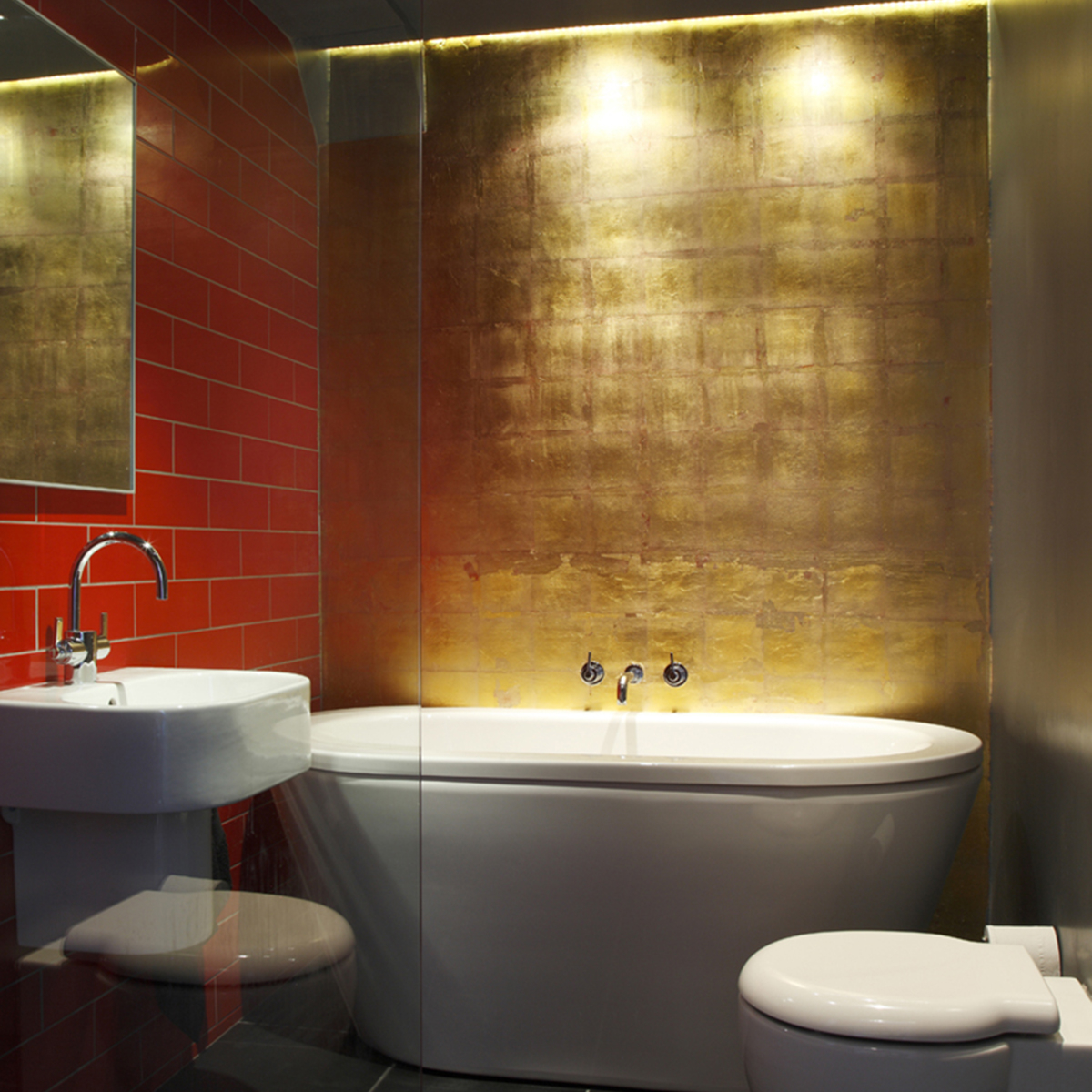 Freestanding modern bath with gold and red metro brick walls.