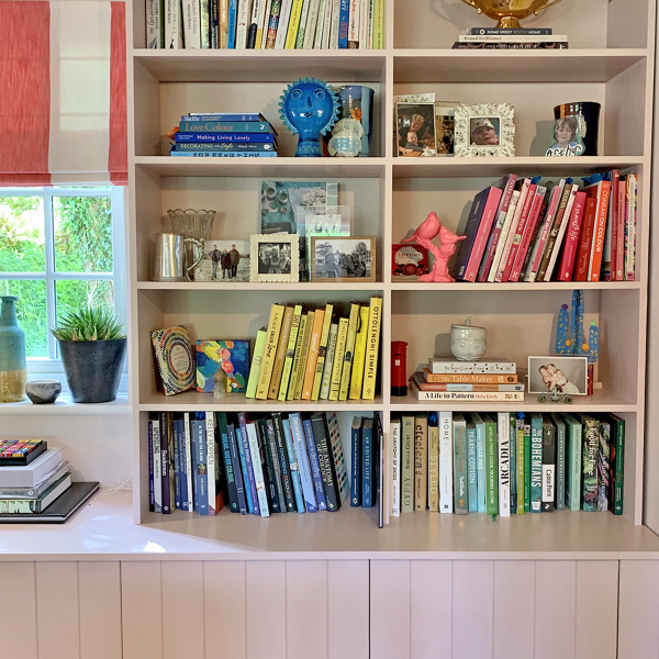 open bookshelves in pale pink with colour coded books and objets.