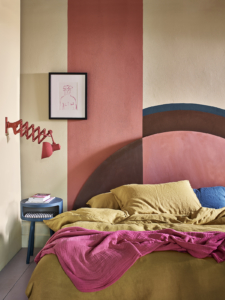 pink and brown circular headboard with colour block painting behind, mustard bedlinen and red wall light