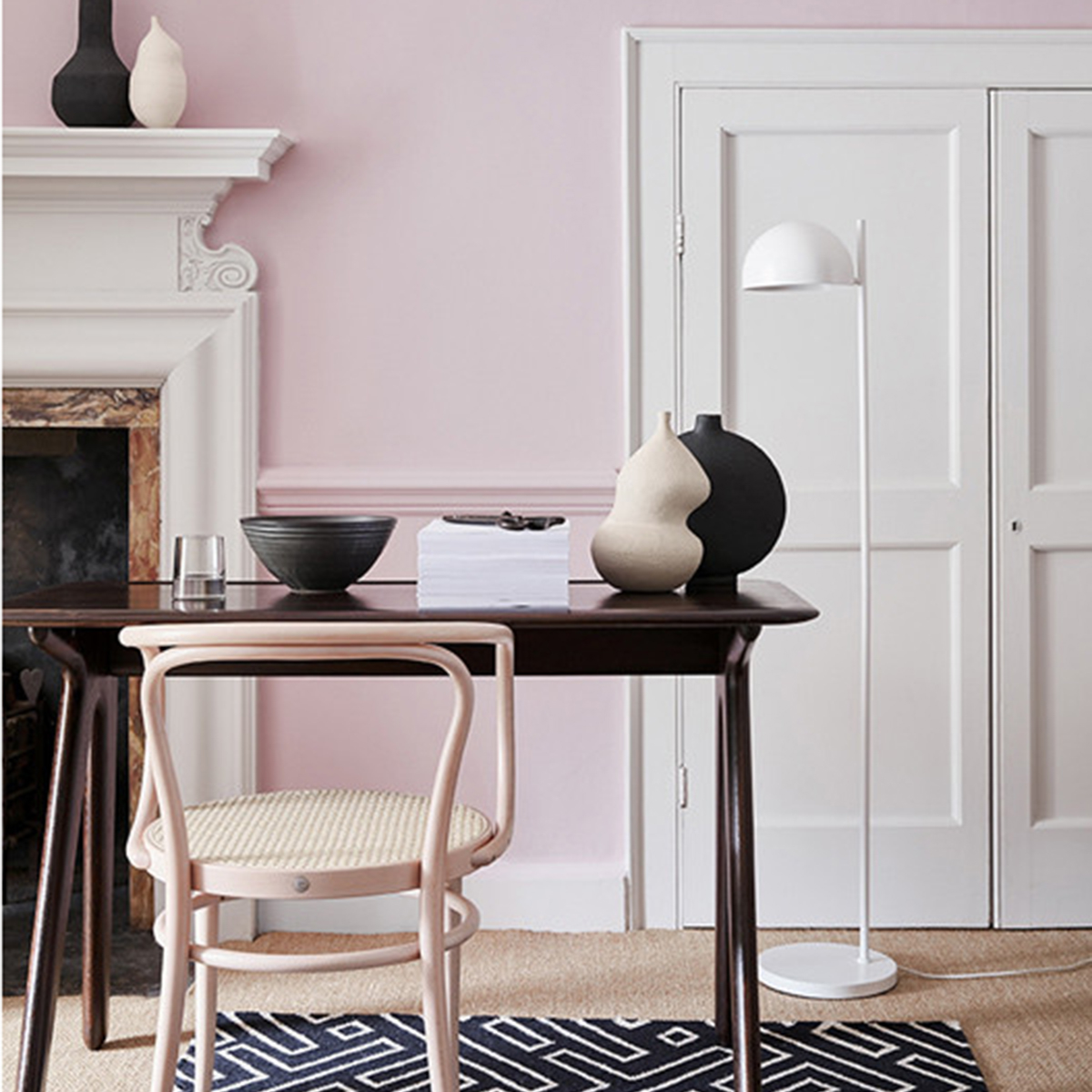 Pale pink walls, white floor lamp, black desk, pale wood chair and monochrome geometric rug. Image by Little Greene