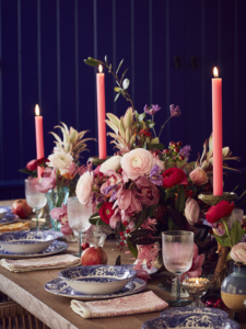 Christmas dining table with large pink, red and orange floral centrepiece, pink dinner candles and blue patterned Spode tableware in the home of Sophie Robinson
