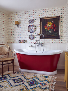 red painted roll top bath, vintage Moroccan rug, spot and waves patterned wallpaper, vintage framed art in the bathroom of Sophie Robinson