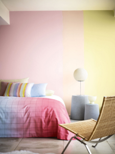 Ombre effect painted bedroom wall in pale pink, peach and yellow. Pinka nd blue ombre bedlinen and woven chair. Image by Dulux