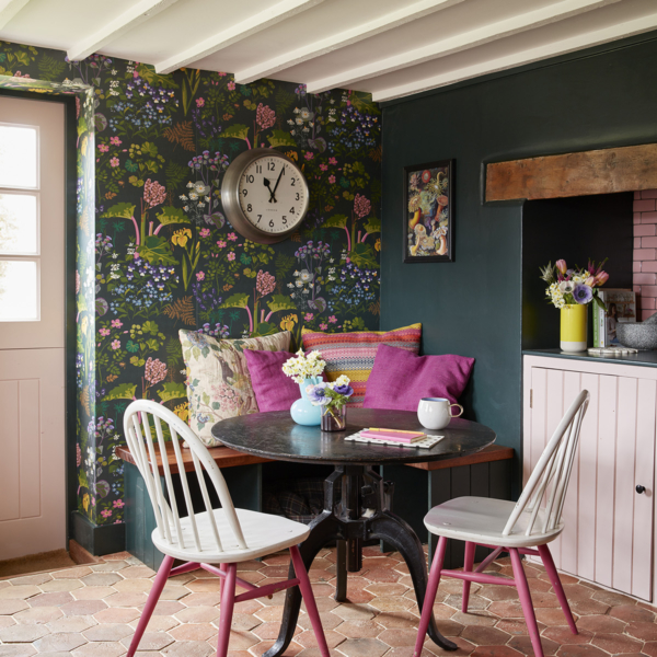 Green colourful botanical print wallpaper, dark green wall, small black round table and white and pink dining chairs. Sophie Robinson's kitchen