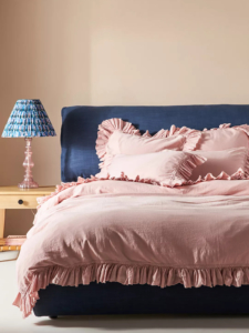 Navy blue upholstered bed and pale pink bedlinen with frill edge. Image by Anthropologie