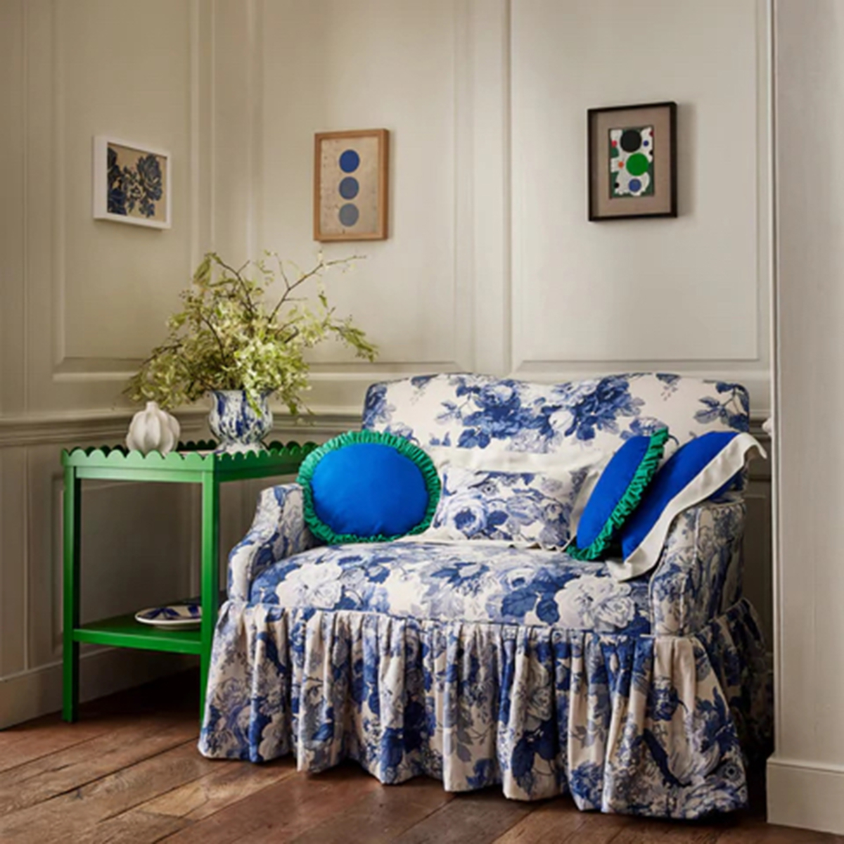 Stone coloured panelled wall, blue and white floral statement loveseat with large ruffle trim, green scallop top side table