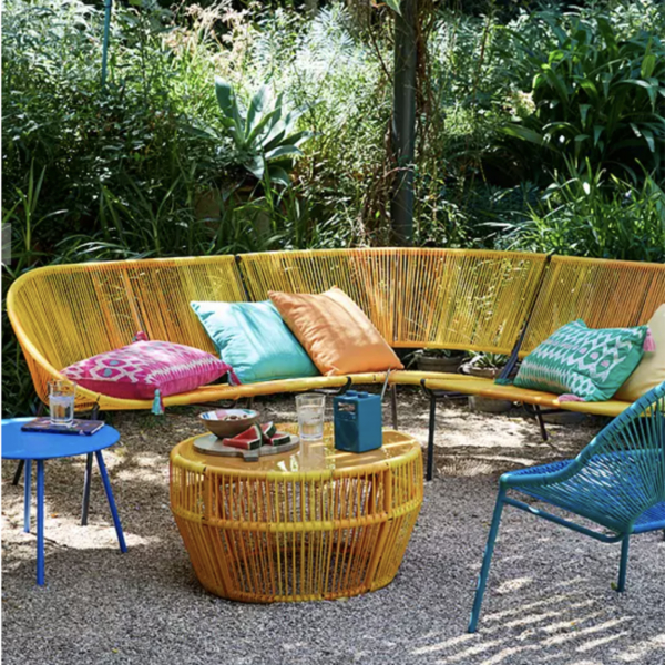 Corner woven outdoor sofa in yellow with matching coffee table and blue dining chairs. Sophie Robinson