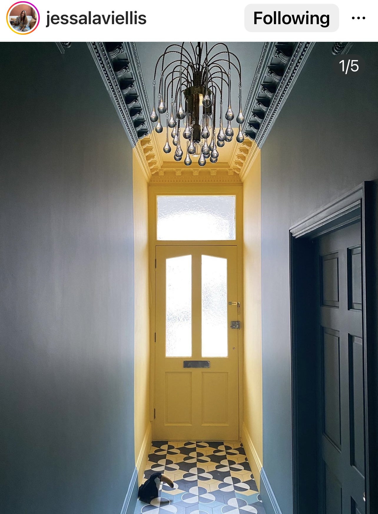 Small entrance hallway with bright yellow front door and dark painted dark grey walls and patterned cement tiles on floor