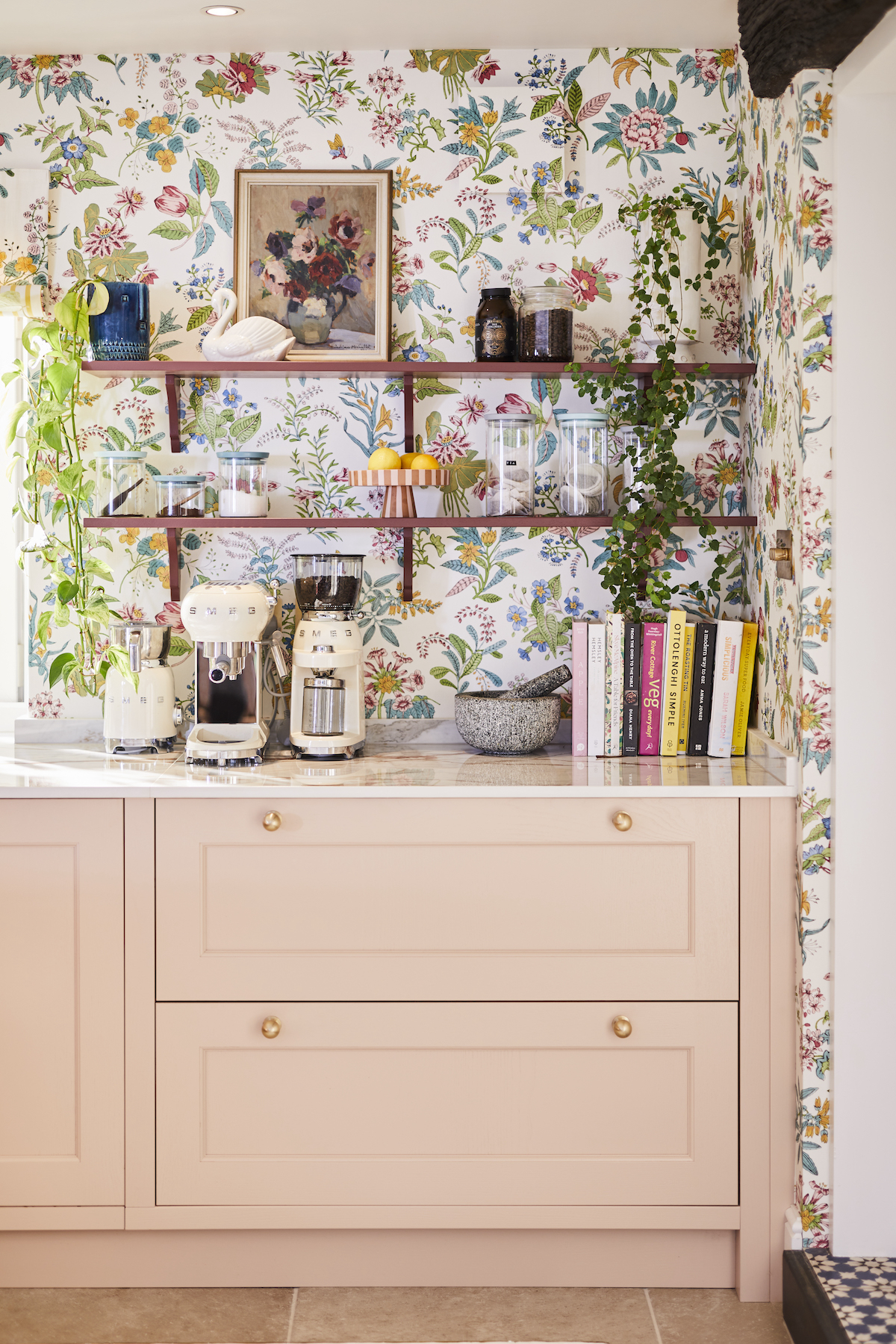 Kitchen cabinet in Chalk Blush Pink with white worktop and open shelving in Burlington Red. Shelves display a range of artwork, plants and glass storage jars with cookbooks and small Smeg appliances underneath.