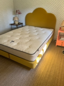 Vibrant saffron yellow velvet headboard and bed base with new bare mattress on it and no bedding.