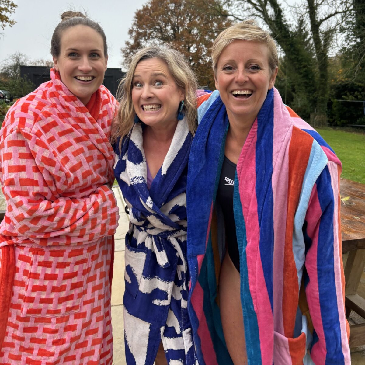 Three white women wearing colourful bathrobes and excited faces having just done an ice bath.