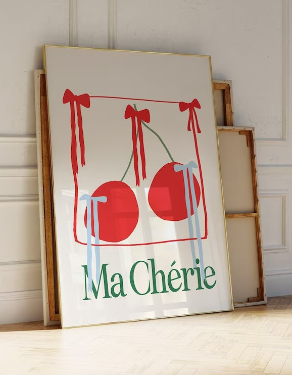Large poster with white background, red cherries in the centre with red and light blue ribbon prints adorning it. Print has Ma Cherie in bold green type at the bottom.